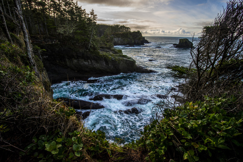 Cape Flattery coastal bluff with crashing turquoise waves, sea stacks, and overcast sky